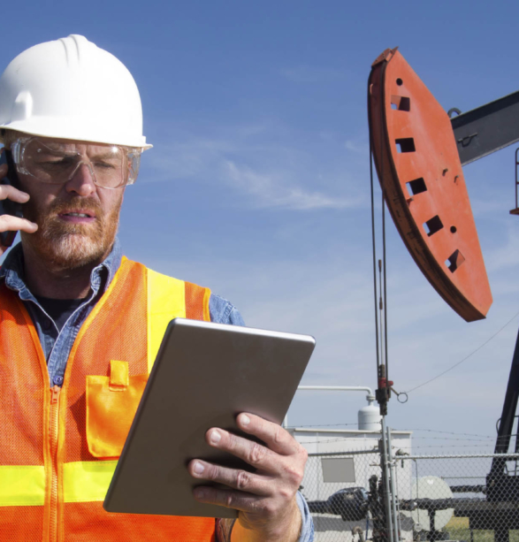 A royalty free image from the oil and gas industry of an oil engineer at a pumpjack using a tablet PC and cellular.